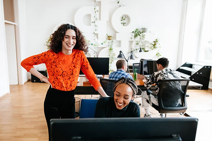 two female business owners, one standing over the other looking at the a computer screen